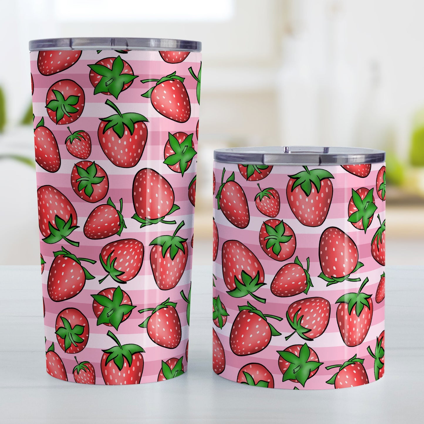 Strawberries on Pink Stripes Tumbler Cup (20oz and 10oz, stainless steel insulated) at Amy's Coffee Mugs. A tumbler cup featuring a print of hand-drawn strawberries in red and green in an assorted pattern over a pink stripes background that wraps around the cup. Photo shows both sized cups on a table next to each other.