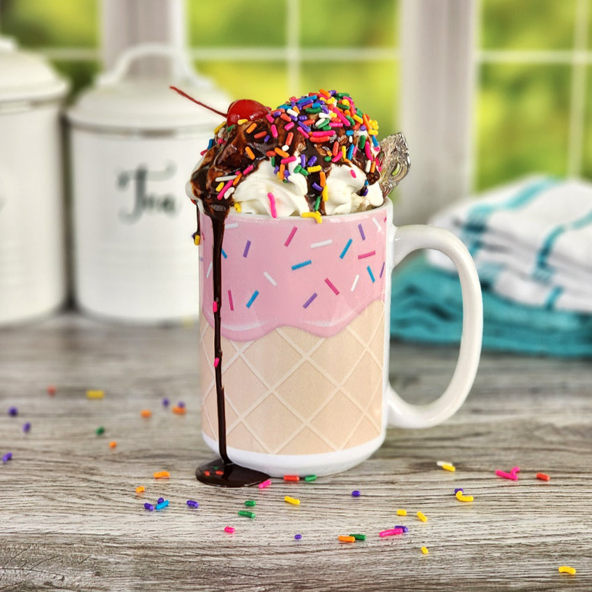 Strawberry Ice Cream Waffle Cone Mug with ice cream in it - Amy's Coffee Mugs. A ceramic coffee mug with a yummy looking dessert illustration of pink strawberry ice cream with sprinkles atop a waffle cone pattern in a design that wraps around the mug up to the handle.