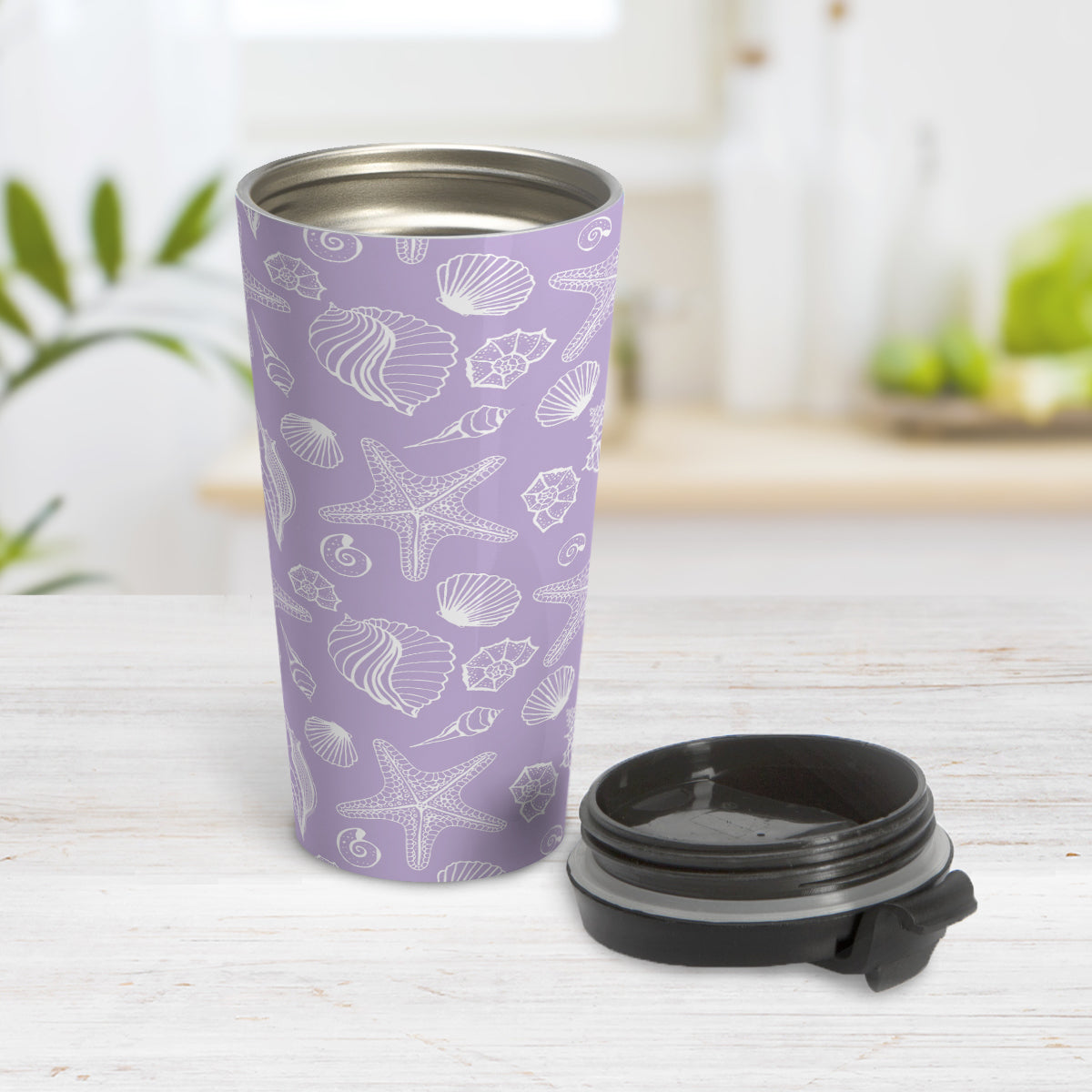 White Seashell Pattern Purple Beach Travel Mug (15oz) at Amy's Coffee Mugs. A travel mug designed with a white seashell line drawing pattern over a purple background that wraps around the travel mug. Photo shows the open travel mug with the lid on the table beside it.