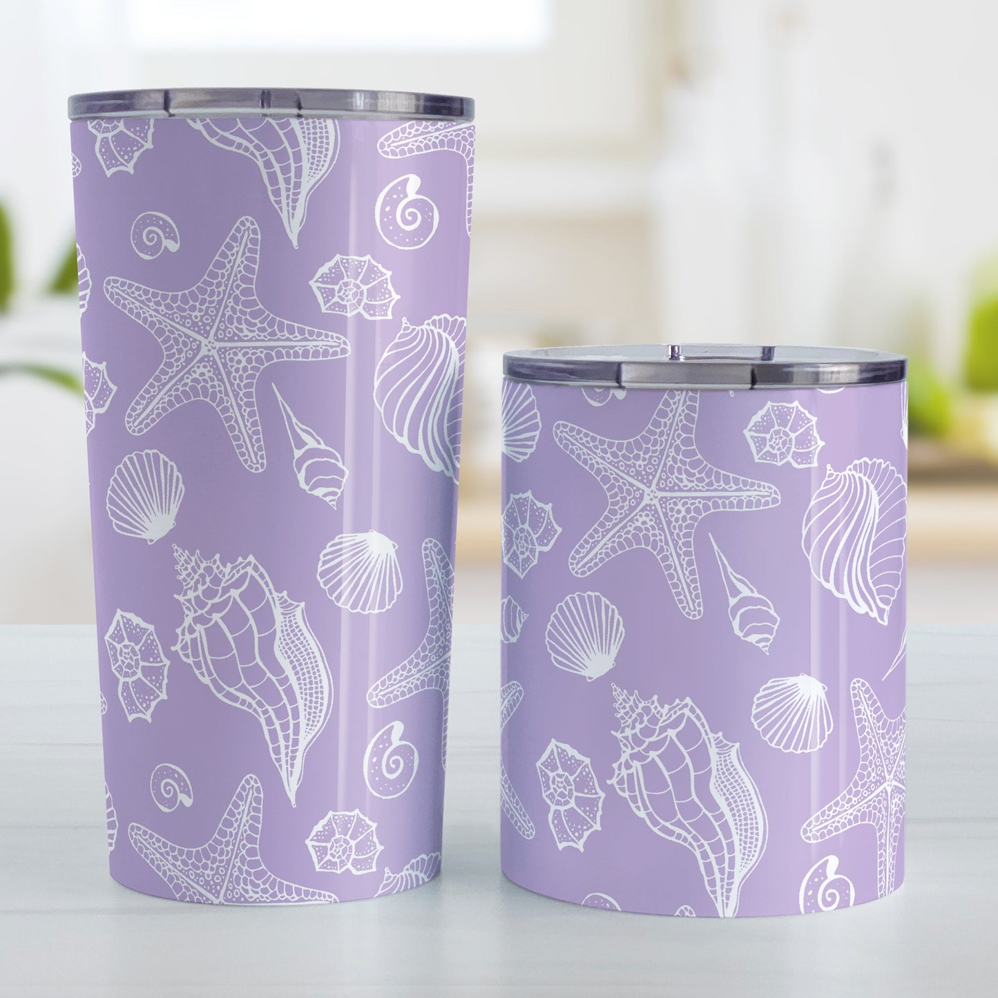 White Seashell Pattern Purple Beach Tumbler Cup (20oz and 10oz, stainless steel insulated) at Amy's Coffee Mugs. Tumbler cups designed with a white seashell line drawing pattern over a purple background that wraps around the cups. Photo shows both sized cups on a table next to each other.
