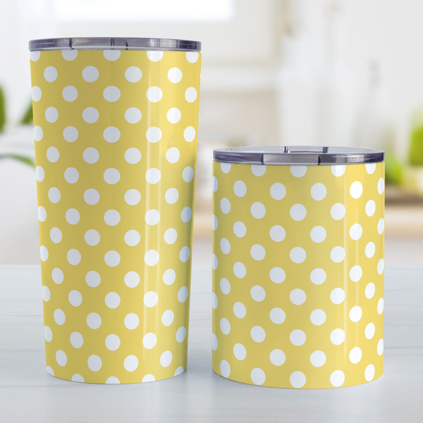 Yellow Polka Dot Tumbler Cup (20oz and 10oz, stainless steel insulated) at Amy's Coffee Mugs. Tumbler cups designed with a pattern of white polka dots over a yellow background color that wraps around the cups. Photo shows both sized cups on a table next to each other.