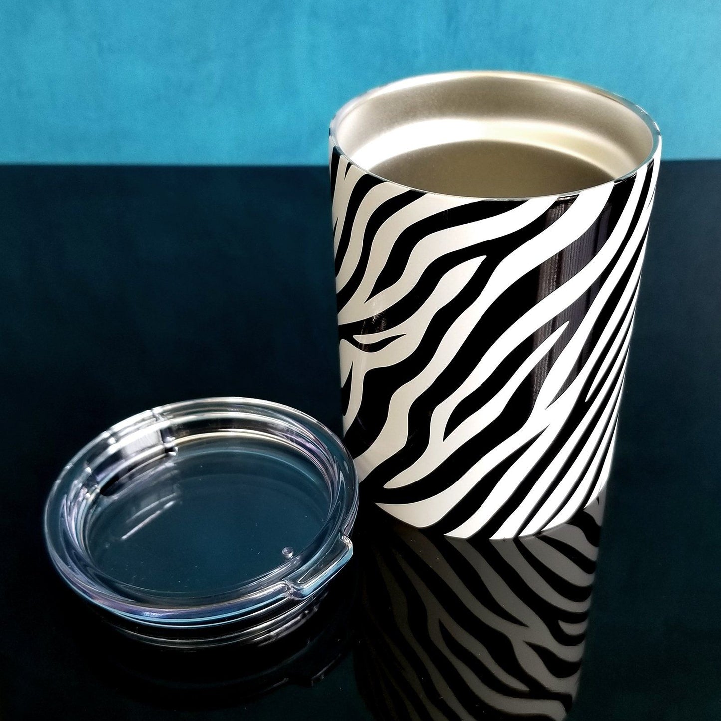 Zebra Print Pattern Tumbler Cups (10oz) with lid open on blue and glossy black background - Amy's Coffee Mugs. A stainless steel tumbler cup with an animal print pattern of black and white zebra stripes that wraps around the cup.