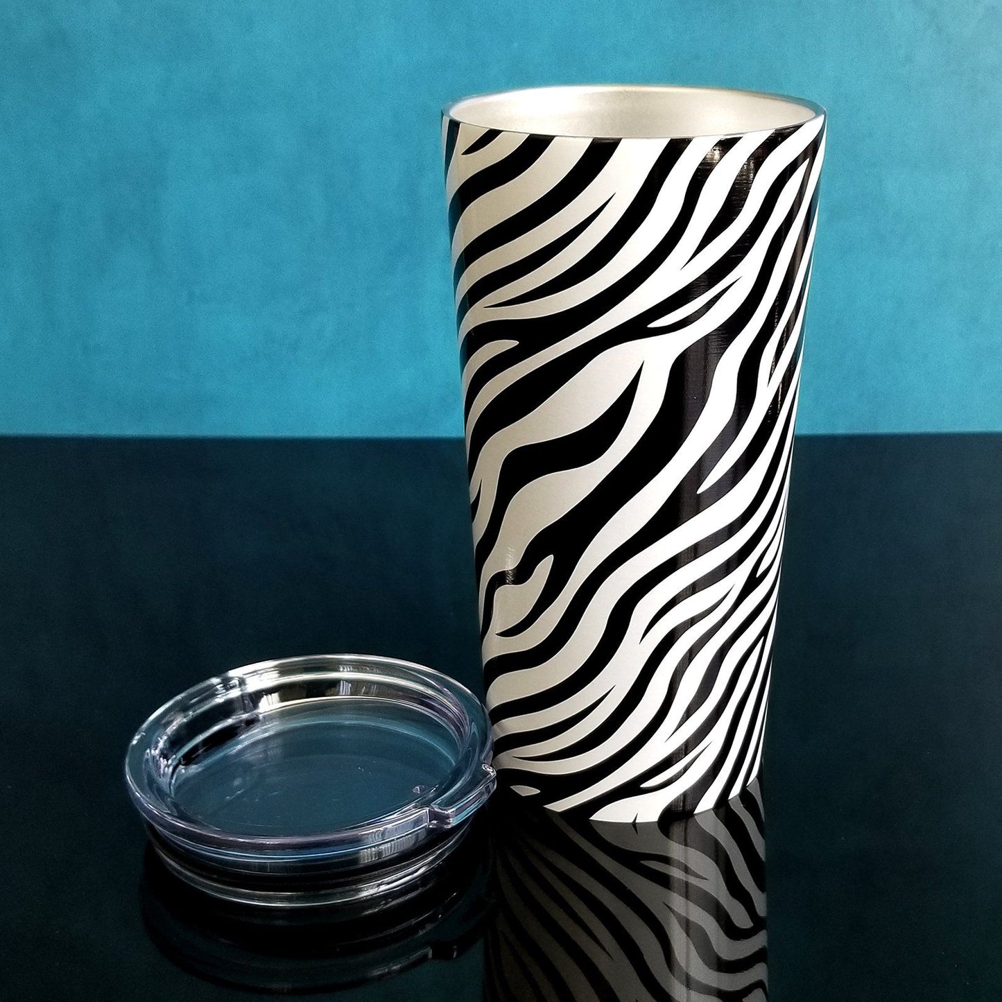 Zebra Print Pattern Tumbler Cups (20oz) with lid open on blue and glossy black background - Amy's Coffee Mugs. A stainless steel tumbler cup with an animal print pattern of black and white zebra stripes that wraps around the cup.