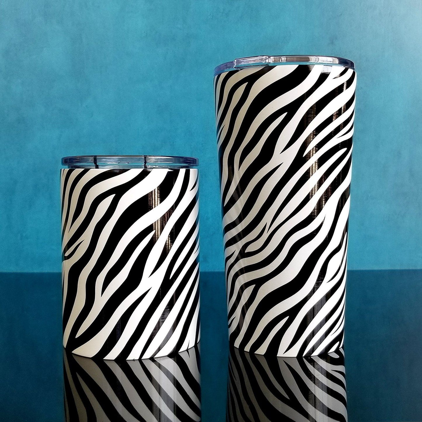 Zebra Print Pattern Tumbler Cups (10oz and 20oz) on blue and glossy black background - Amy's Coffee Mugs. A stainless steel tumbler cup with an animal print pattern of black and white zebra stripes that wraps around the cup.