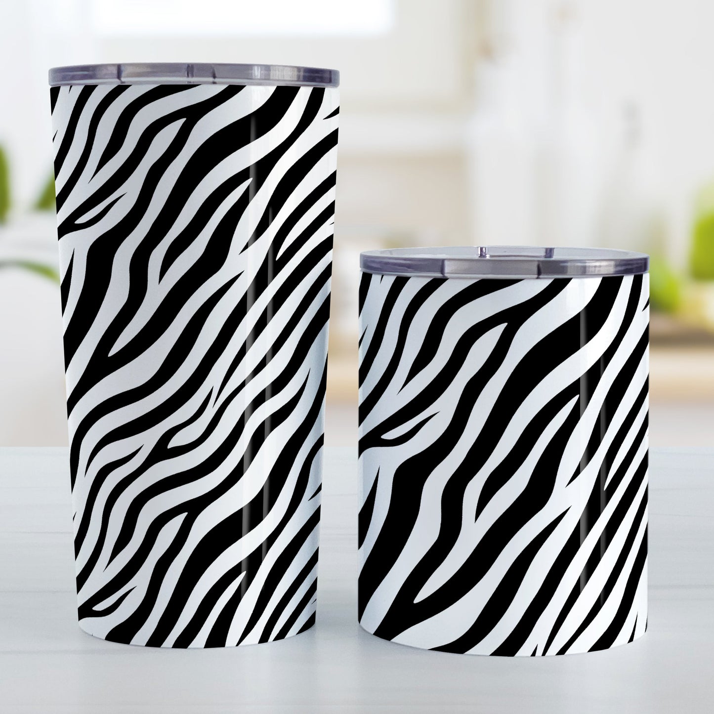 Zebra Print Pattern Tumbler Cup (20oz and 10oz, stainless steel insulated) at Amy's Coffee Mugs. Stainless steel tumbler cups with an animal print pattern of black and white zebra stripes that wraps around the cups. Photo shows both sized cups on a table next to each other.