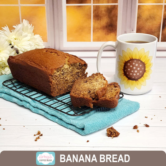 Banana bread on a table next to a sunflower mug in front of a window with an autumn scene.