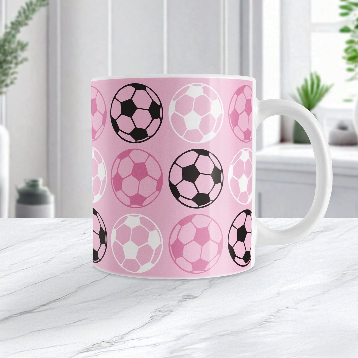 White 11oz mug with pink background and soccer ball pattern, on a marble tabletop