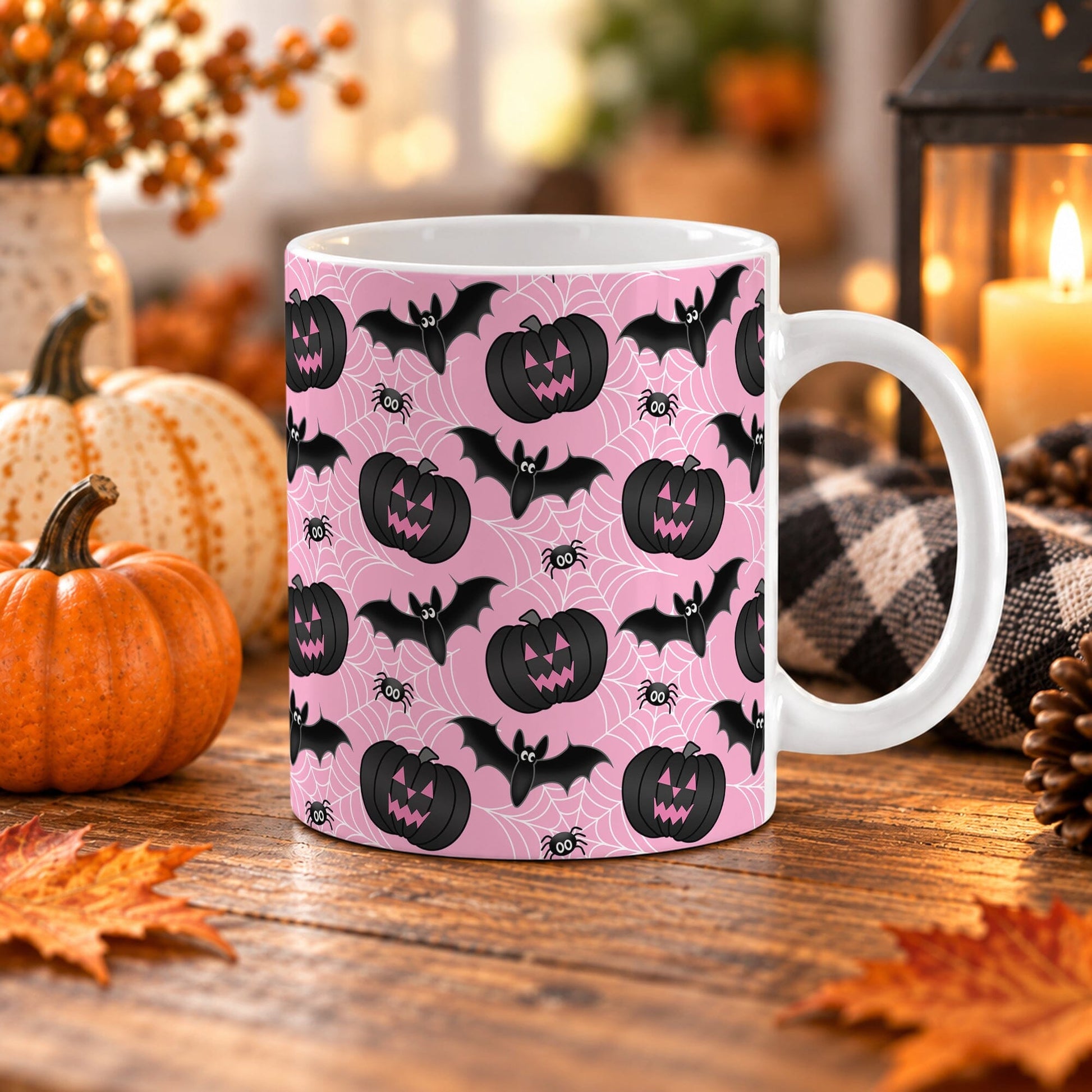 White 11 oz ceramic Halloween mug with black jack-o'-lanterns, bats, spiders, and white spider webs on a pink background, sitting upon a wooden table with fall decor around it.