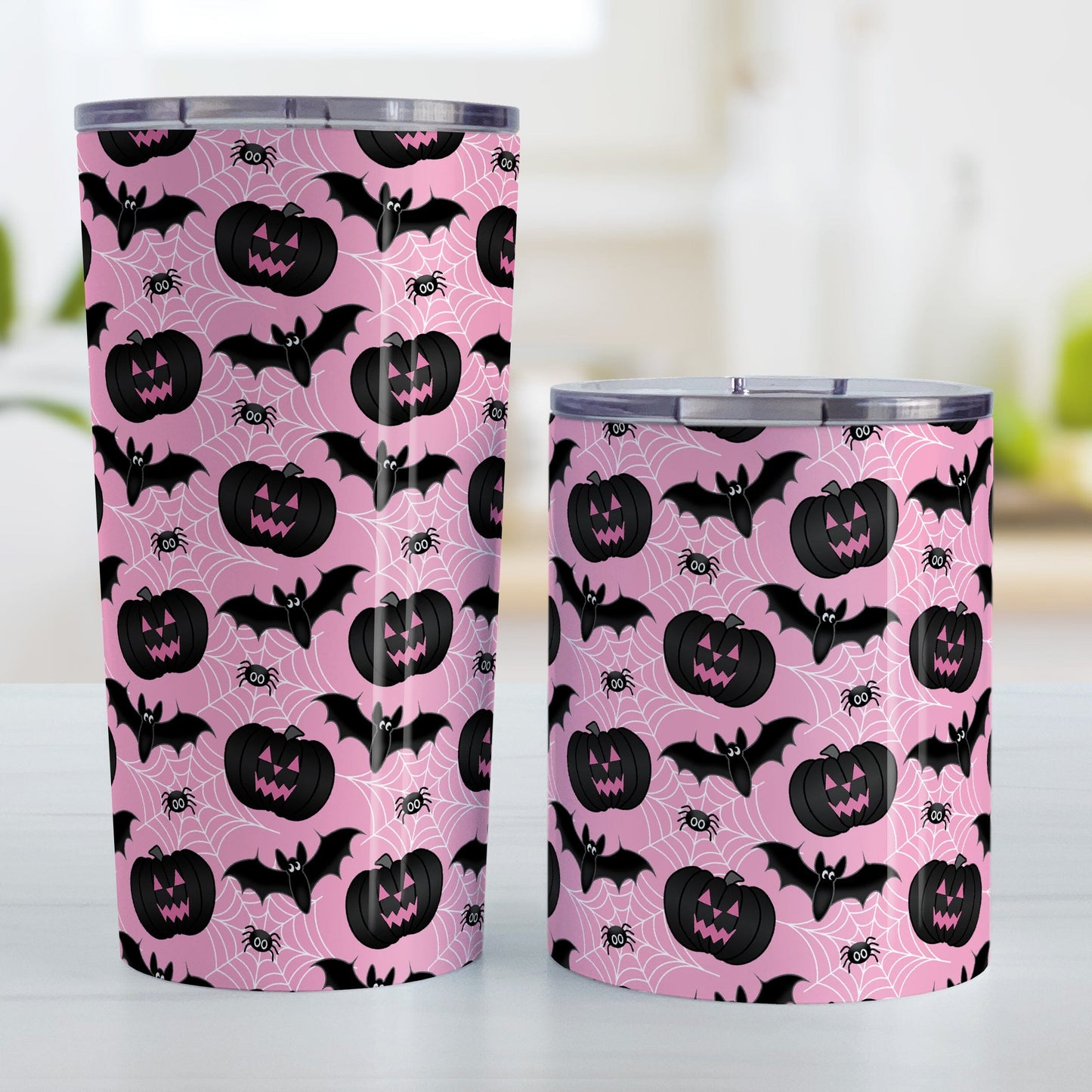 Black Pumpkins Bats and Spiders Pink Halloween Tumbler Cup (20oz or 10oz) at Amy's Coffee Mugs. A tumbler cup designed with a pattern of black carved pumpkins, bats, and spiders in their webs in a pattern over a pink background color that wraps around the cup. Photo shows both sized cups on a table next to each other.