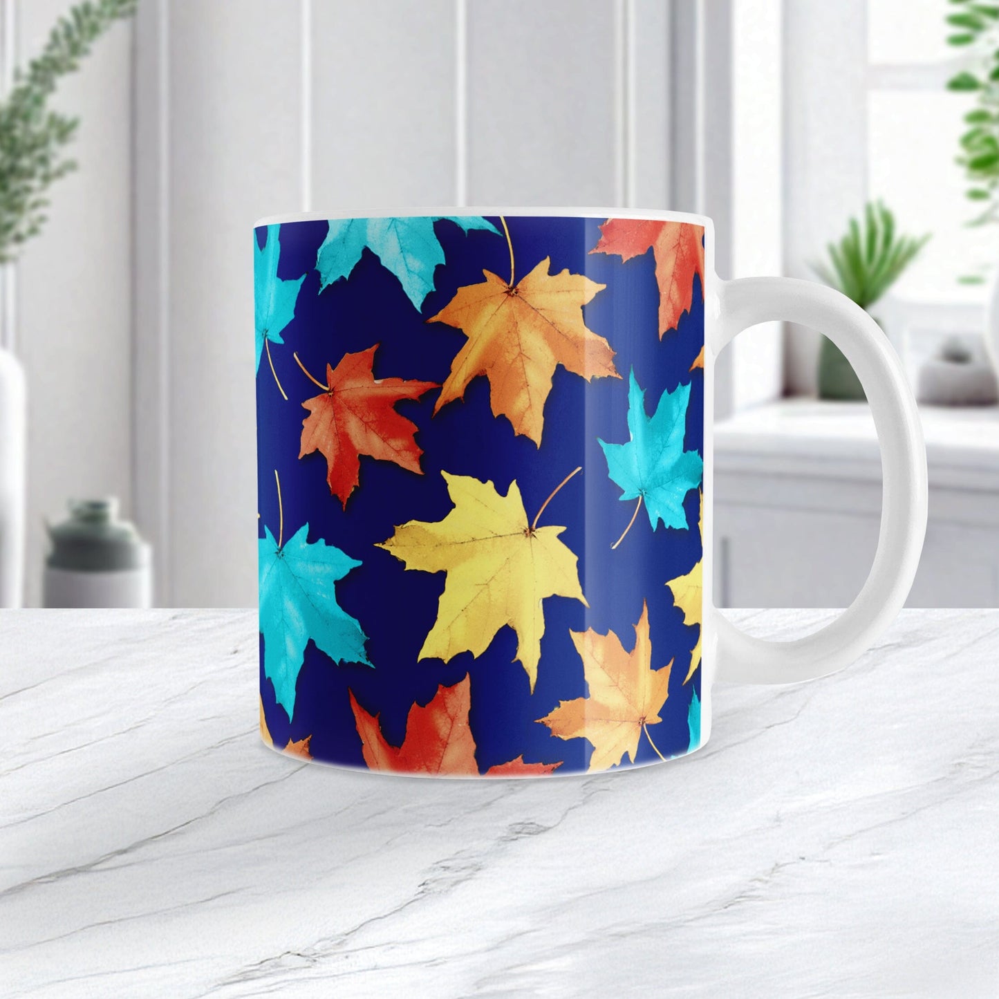 11 oz Blue Fall Leaves Mug with colorful turquoise, orange, and yellow autumn leaves over a deep navy blue background, on a marble countertop in a bright white kitchen.