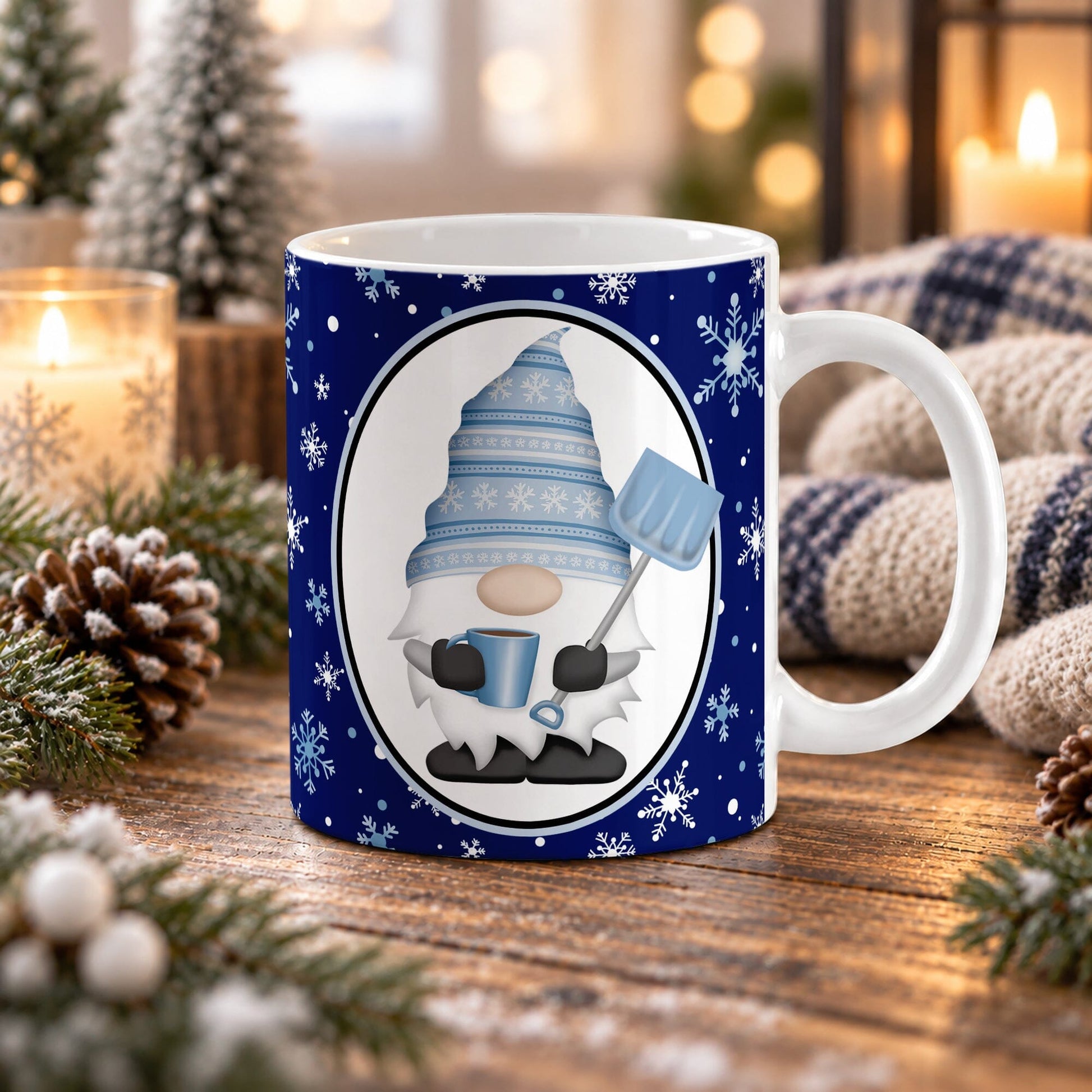 An 11 oz white ceramic mug with a navy blue holiday and winter gnome design, placed on a wooden table surrounded by cozy Christmas decorations like pinecones, evergreen branches, and a knitted blanket.