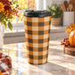 15 oz brown and orange buffalo plaid travel mug with brown, orange, and beige buffalo check pattern, on a granite countertop in a kitchen with fall decor including autumn plants, a pumpkin, and an orange plaid tea towel.