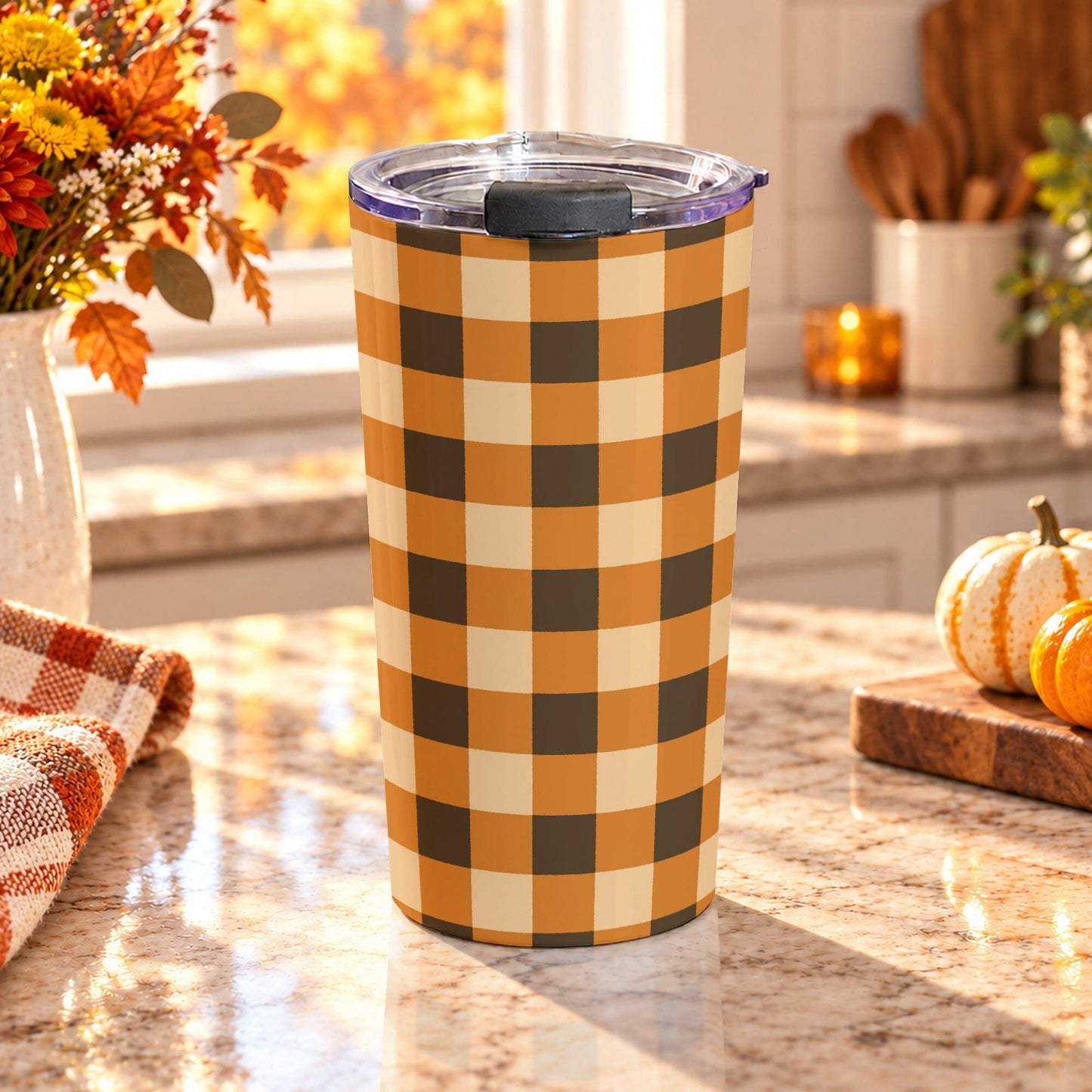20 oz brown and orange buffalo plaid tumbler cup with brown, orange, and beige buffalo check pattern, on a granite countertop in a kitchen with fall decor including autumn plants, pumpkins, and an orange plaid tea towel.