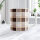 11 oz brown orange plaid mug with dark brown, light brown, white, and warm orange layered plaid pattern, on a marble countertop in a white kitchen.