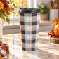 15 oz brown and orange plaid travel mug with dark brown, light brown, white, and orange layered plaid pattern, on a granite countertop in a kitchen with fall decor including autumn plants, a pumpkin, and an orange plaid tea towel.