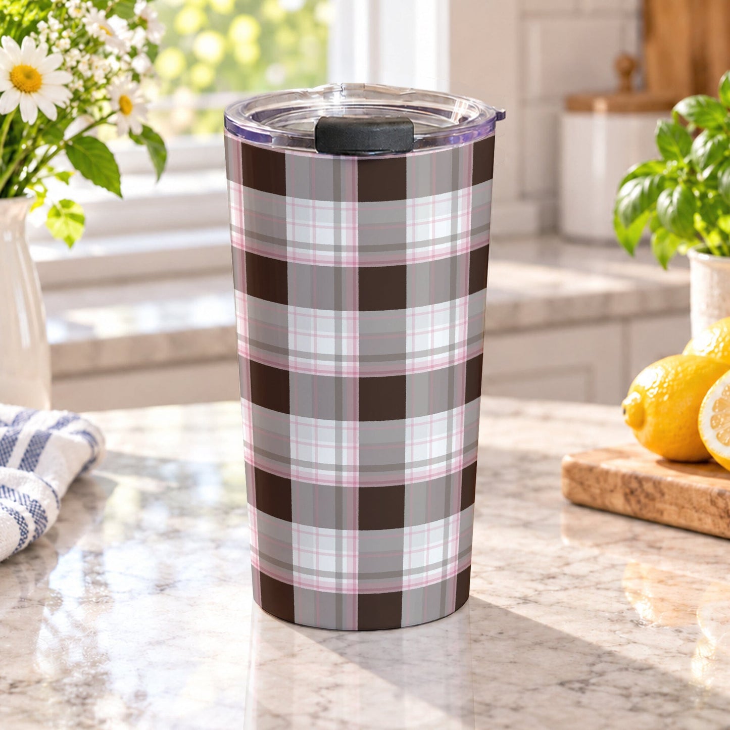 20 oz brown and pink plaid tumbler cup with a brown, taupe, white, and soft pink pattern, on a granite countertop in a bright kitchen with spring/summer daisies, green plants, tea towel, and lemons on a wood cutting board.