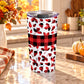 20 oz fall tumbler cup with red and black buffalo plaid, assorted autumn leaf shapes, and a wide checkered band around the center, on a granite countertop in a kitchen with fall decor including autumn plants, pumpkins, and an orange plaid tea towel.