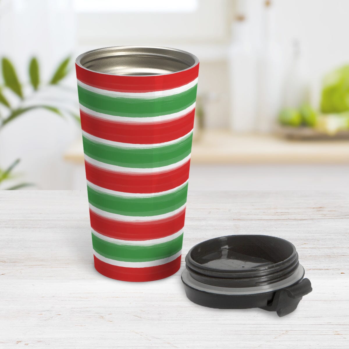 Christmas Paint Brush Strokes Travel Mug (15oz) at Amy's Coffee Mugs. A stainless steel travel mug featuring a print of artistic paint brush strokes horizontally across the travel mug in alternating colors of red and green to celebrate the Christmas holiday. Photo shows the mug open with the lid on the table beside it.