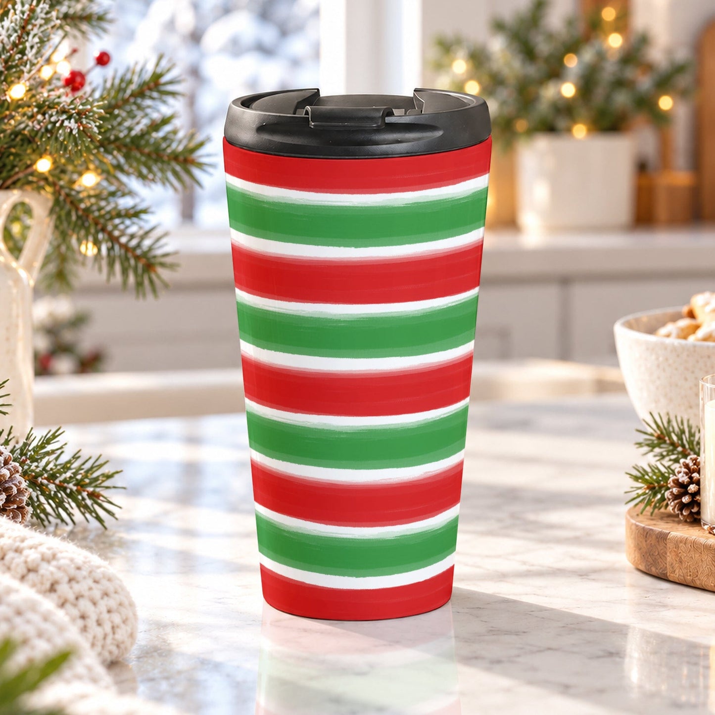15 oz Christmas travel mug with red and green painted brushstroke stripes wrapping around the insulated stainless steel cup, on a granite countertop in a bright kitchen with light rustic winter decor around it.
