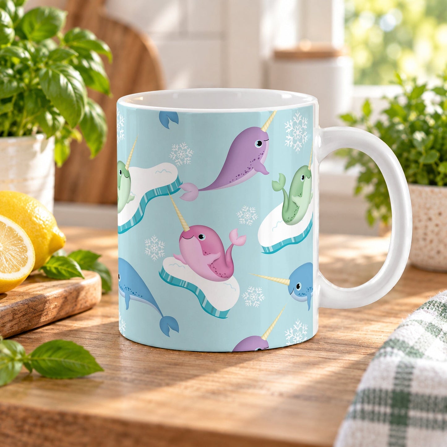 11 oz colorful narwhal mug with pink, purple, blue, and green narwhals, snowflakes, and icy details on a light blue background, on a wooden countertop in a bright kitchen with green plants, a plaid tea towel, and lemons on a wood cutting board.