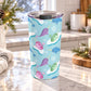 Colorful narwhal tumbler cup with pink, purple, blue and green narwhals, snowflakes, icy shapes, and a 20 oz insulated stainless steel body, on a granite countertop in a bright kitchen with light rustic decor including pine cones, pine boughs, lights, and a cozy blanket.