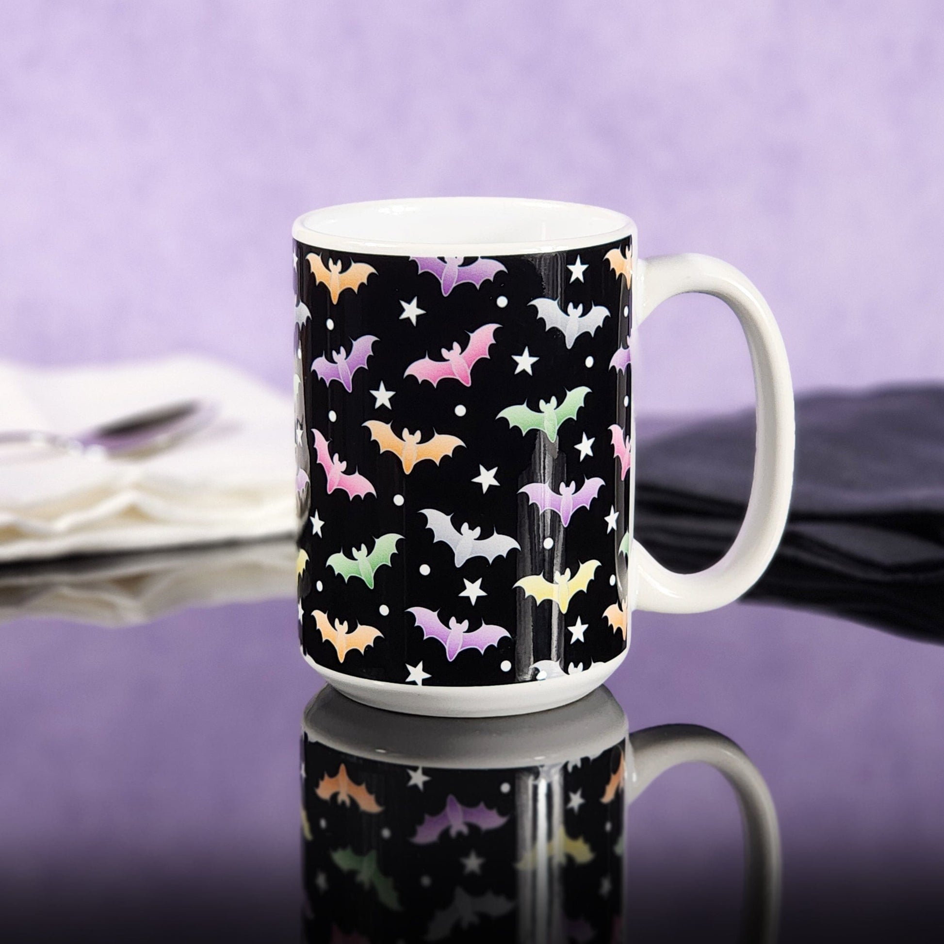 Colorful Bats Mug (15oz) at Amy's Coffee Mugs. Photo shows the mug on a glossy black tabletop with a purple wall background.