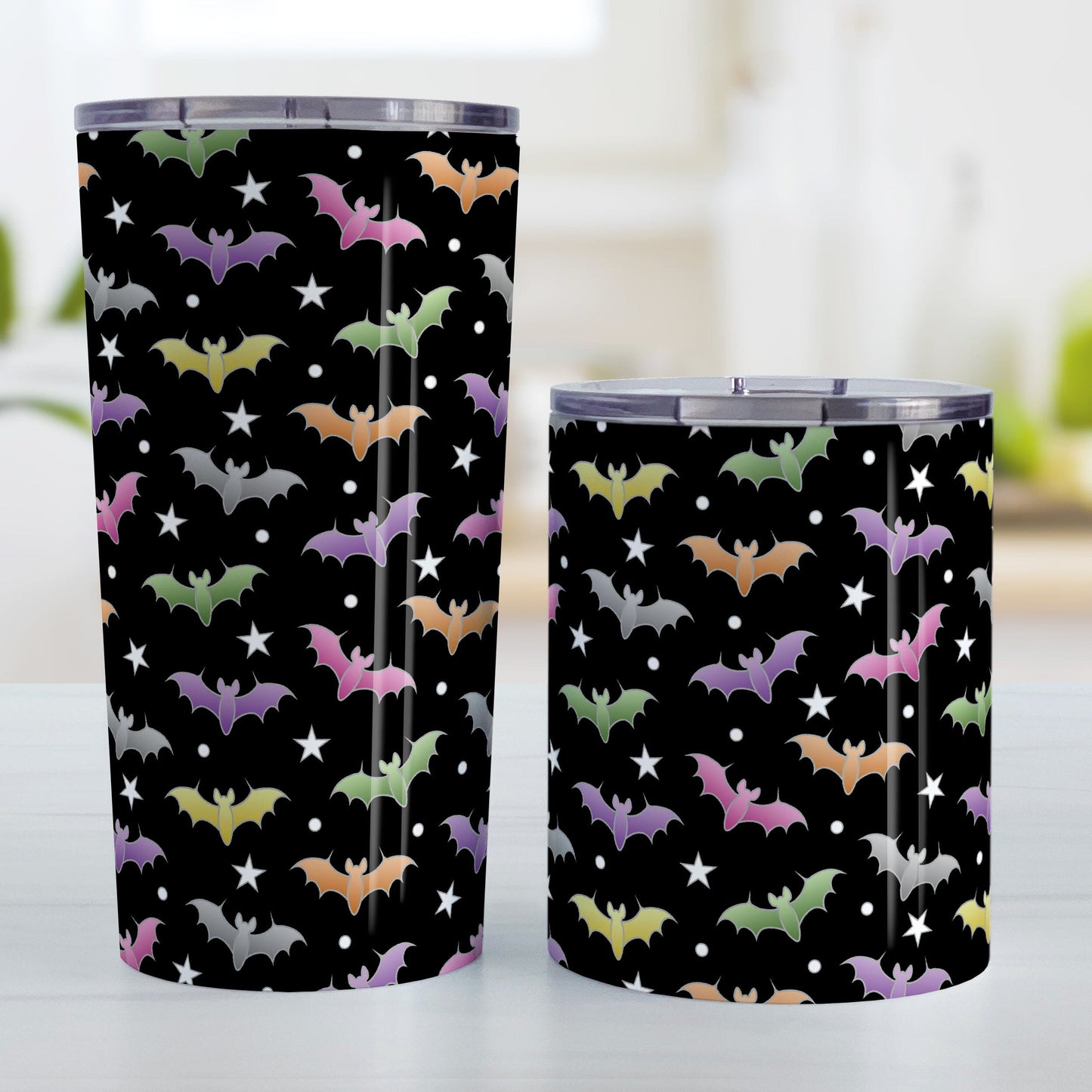 Colorful Bats Tumbler Cup (20oz or 10oz) at Amy's Coffee Mugs. A tumbler cup designed with different colored bats and stars in an assorted pattern over a black background color that wraps around the cup. Photo shows both sized cups on a table next to each other.