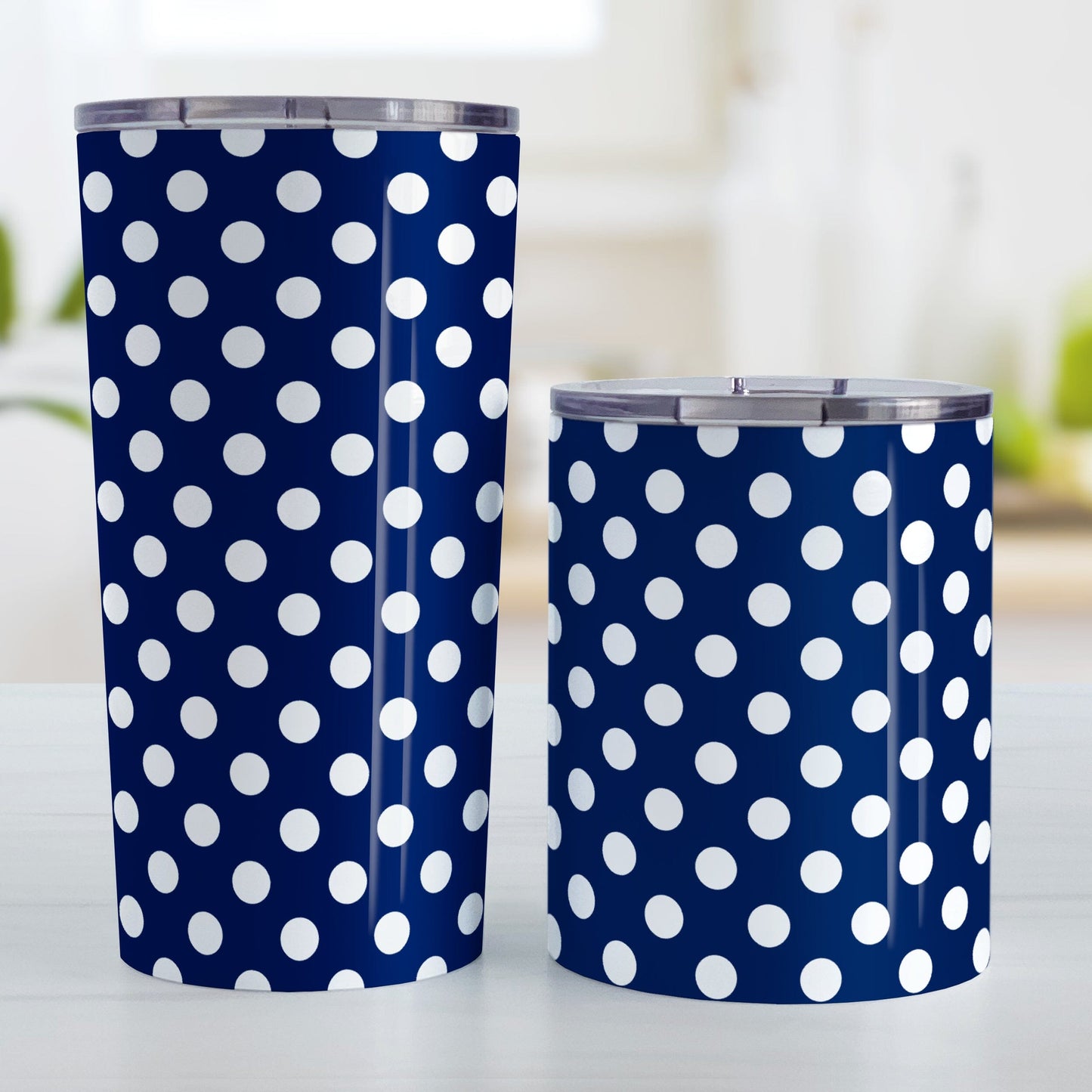 Dark Blue Polka Dot Tumbler Cup (20oz and 10oz, stainless steel insulated) at Amy's Coffee Mugs. Cups designed with a pattern of white polka dots over a dark navy blue background color that wraps around the cups. Photo shows both sized cups on a table next to each other.