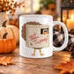 11 oz funny Thanksgiving turkey mug with cartoon turkey hiding in a cardboard box labeled “Not a Turkey!” in red lettering, on a wooden table in a fall-themed setting with pumpkins, autumn leaves, and a candle.