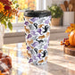15 oz stainless steel Halloween travel mug with purple, orange, black, and gray ghosts and spirits on white with a black screw-on lid, on a marble countertop in a kitchen with fall decor including autumn plants, a pumpkin, and an orange plaid tea towel.