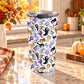 20 oz insulated stainless steel Halloween tumbler cup with purple, orange, black, and gray ghosts and spirits on a white background, on a granite countertop in a kitchen with fall decor including autumn plants, pumpkins, and an orange plaid tea towel.
