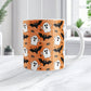 Halloween-themed mug with ghost, bat, and spider pattern on an orange background. Photo shows the mug on a marble tabletop.