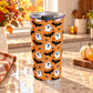 20 oz insulated stainless steel Halloween tumbler cup with white ghosts, black bats, spiders, stars, and white spider webs on an orange background, on a granite countertop in a kitchen with fall decor including autumn plants, pumpkins, and an orange plaid tea towel.