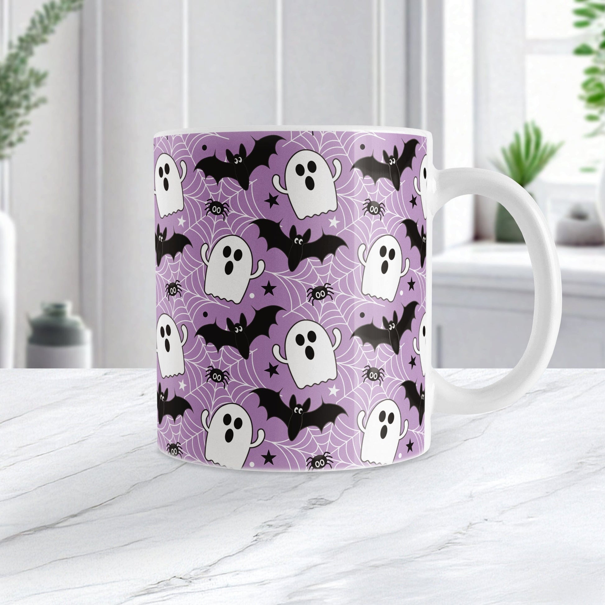 Mug with Halloween pattern featuring ghosts, bats, and spider webs on a purple background. Photo shows the mug on a marble tabletop.