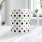 White mug with green, black, and purple polka dots on a white surface.