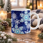 11 oz navy blue winter mug with large aqua and white snowflakes, dark blue snowflakes, and smaller icy accents across the pattern, shown on a wooden table with winter decor around it.