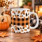 11 oz orange and black buffalo plaid fall mug with assorted plaid autumn leaves and a wide buffalo plaid stripe around the center. The mug is on a wooden table with fall decor around it.