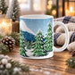 An 11 oz white ceramic mug with a winter mountain and snowy pine tree design, set on a wooden table surrounded by holiday decorations like pinecones, evergreen branches, and a knitted blanket.