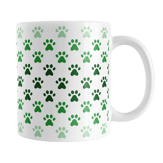 Paw Prints in Green Mug (11oz) at Amy's Coffee Mugs. A ceramic coffee mug designed with paw prints in different shades of green, with the darker green color across the middle and the lighter green along the top and bottom, in a pattern that wraps around the mug to the handle.