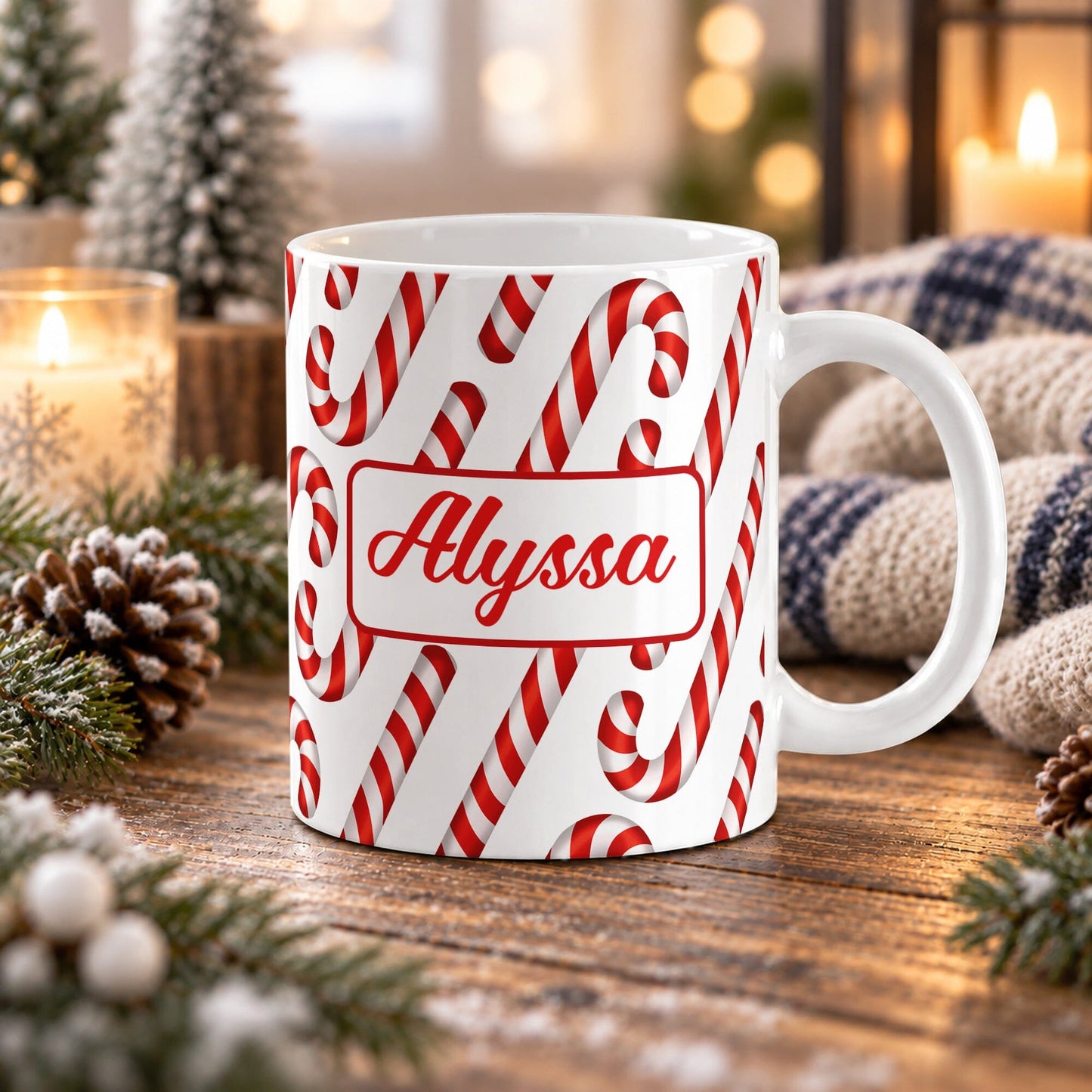 11 oz personalized candy cane pattern mug with red and white candy canes and custom name in red script on both sides, on a wooden table with winter decor around it including pine cones, pine boughs, candles, and a cozy plaid blanket.
