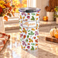 20 oz personalized Changing Leaves Fall Tumbler Cup with colorful autumn leaves and custom name in orange lettering, on a granite countertop in a kitchen with fall decor including autumn plants, pumpkins, and an orange plaid tea towel.