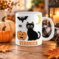 White 11 oz personalized Halloween mug with black cat, jack-o'-lantern, bat, crescent moon, spider web and custom orange name. The mug sits on a wooden table with fall decor around it.