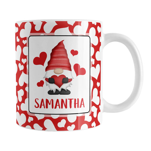 Personalized Cute White Hearts Red Gnome Mug (11oz) at Amy's Coffee Mug. A ceramic coffee mug designed with an adorable red gnome holding a red heart in a white rectangle on both sides of the mug over a pattern of cute white hearts over a red background that wraps around the mug to the handle. Your personalized name is custom printed in an all-capital letters red font below the heart-holding gnome.