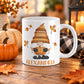 11 oz personalized fall pumpkin gnome mug with orange patterned hat, autumn leaves, and custom name printed below the gnome, displayed on a wooden table with fall decor around it.