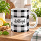 11 oz personalized black and white buffalo plaid mug with custom name in a white framed area, sitting on a wooden table in a bright kitchen with green plants, a tea towel, and lemons on a wood cutting board.
