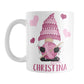 Personalized Pink Crochet Gnome Mug (11oz) at Amy's Coffee Mugs. A ceramic coffee mug designed with a cute gnome wearing a pink crochet hat while holding a ball of pink yarn and a crochet hook with pink hearts around him. Your name is printed in a fun pink font below the gnome. This adorable illustration and personalization is on both sides of the mug. 