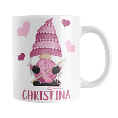 Personalized Pink Crochet Gnome Mug (11oz) at Amy's Coffee Mugs. A ceramic coffee mug designed with a cute gnome wearing a pink crochet hat while holding a ball of pink yarn and a crochet hook with pink hearts around him. Your name is printed in a fun pink font below the gnome. This adorable illustration and personalization is on both sides of the mug. 