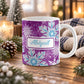 11 oz personalized purple snowflake mug with blue and white snowflakes, aqua blue custom name, and purple winter background, on a wooden table with winter decor around it including pine cones, pine boughs, candles, and a cozy plaid blanket.