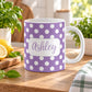 11 oz personalized purple polka dot mug with white dots and custom name in purple script, shown on a wooden table in a bright spring kitchen with green plants and lemons on a cutting board.