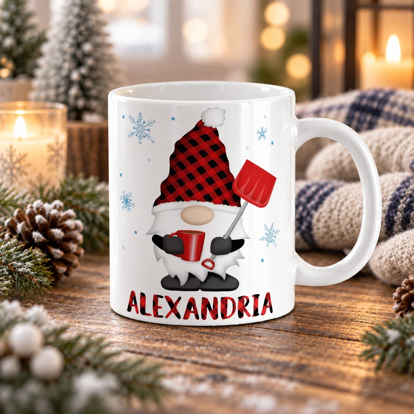 11 oz personalized winter gnome mug with red buffalo plaid hat, red mug, snow shovel, blue snowflakes, and custom plaid name, on a wooden table with winter decor around it including pine cones, pine boughs, candles, and a cozy plaid blanket.
